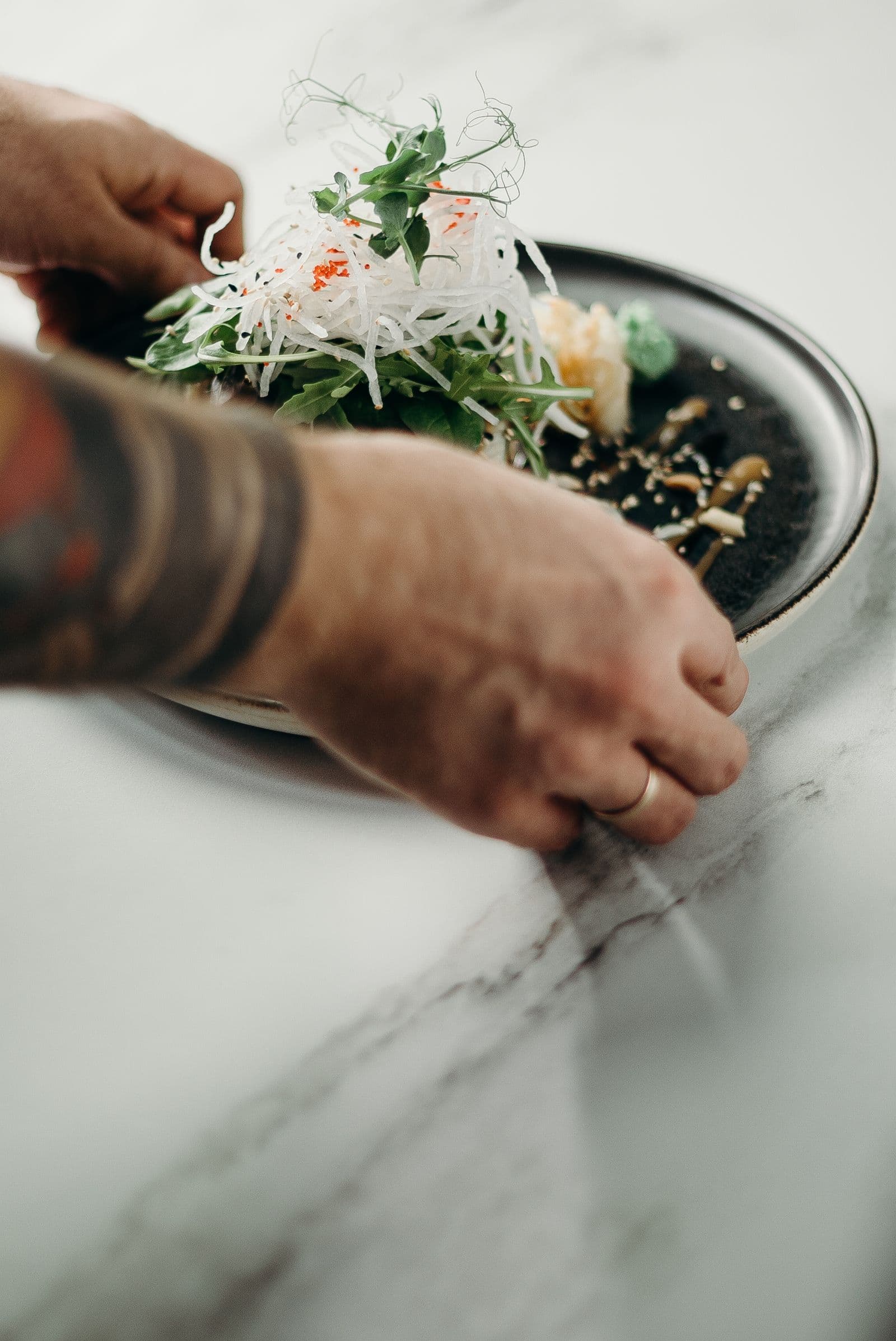 Hands finishing a plated dish on a marble counter
