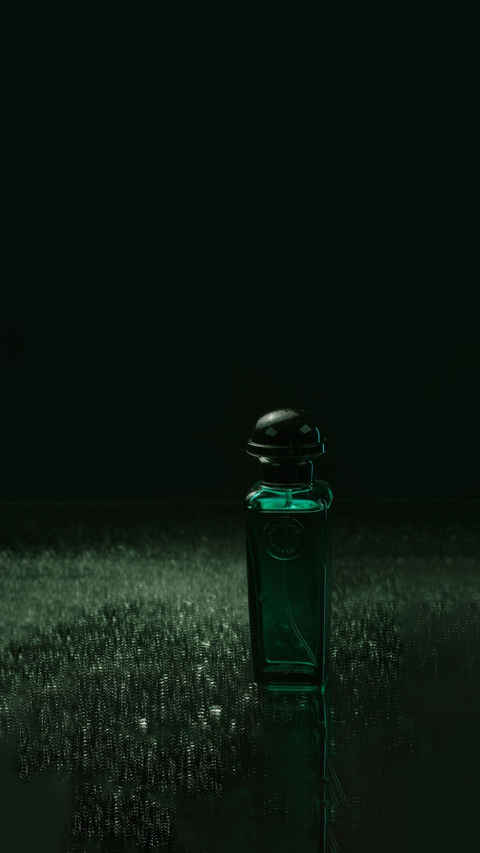 Green glass bottle catching light on a dark reflective surface