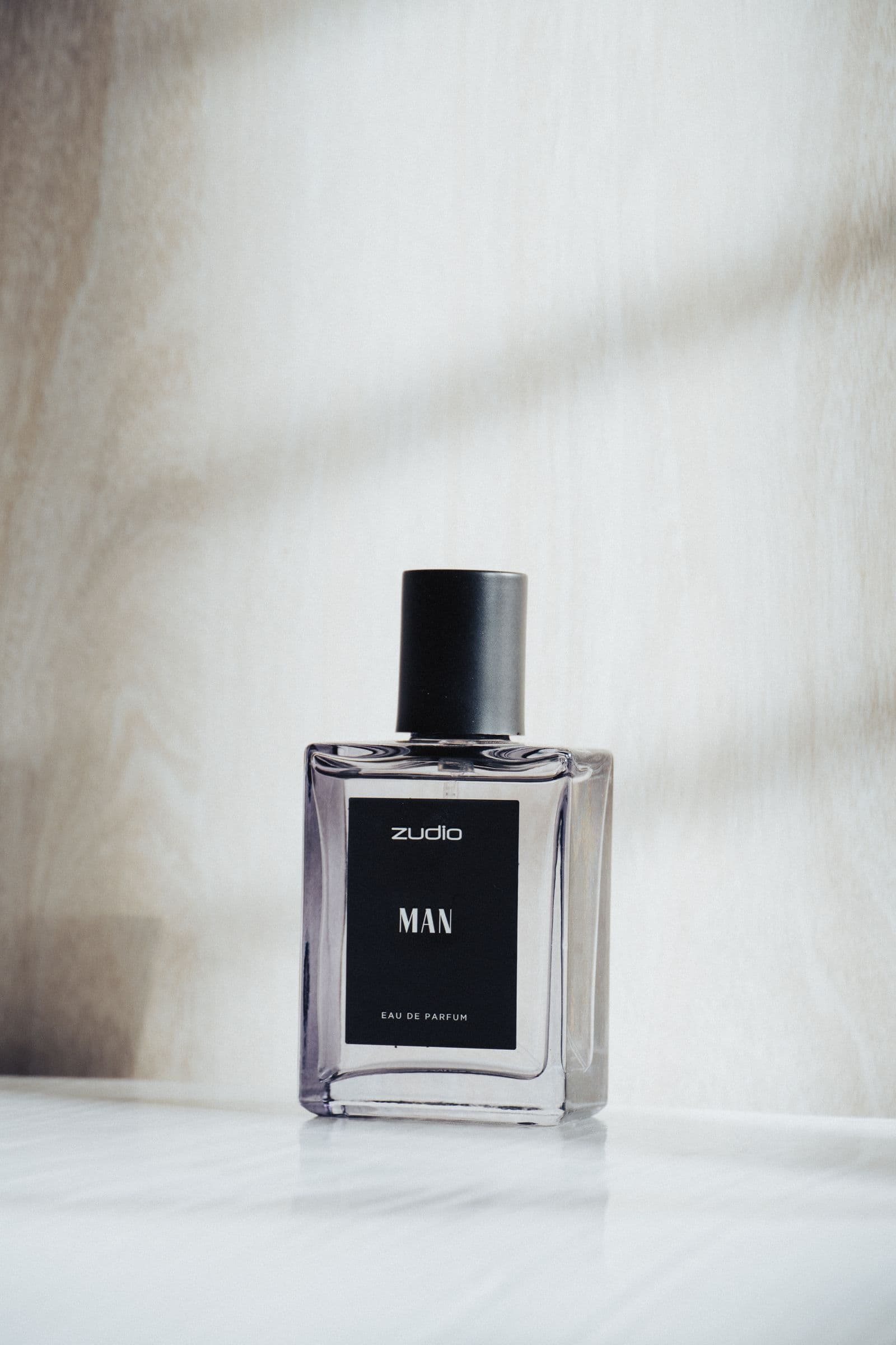 Clear fragrance bottle with a black cap on a white surface in soft window light