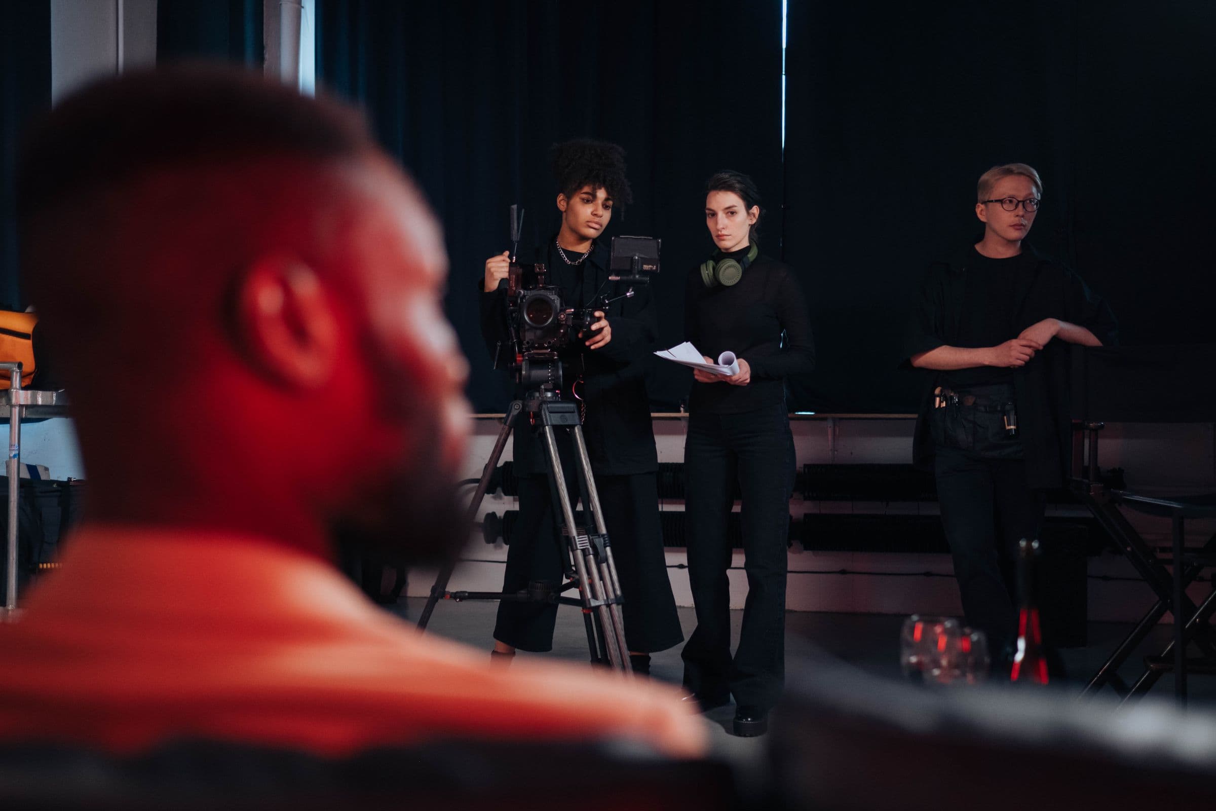 Film crew preparing a scene in a dark studio, a camera operator lit in red in the foreground