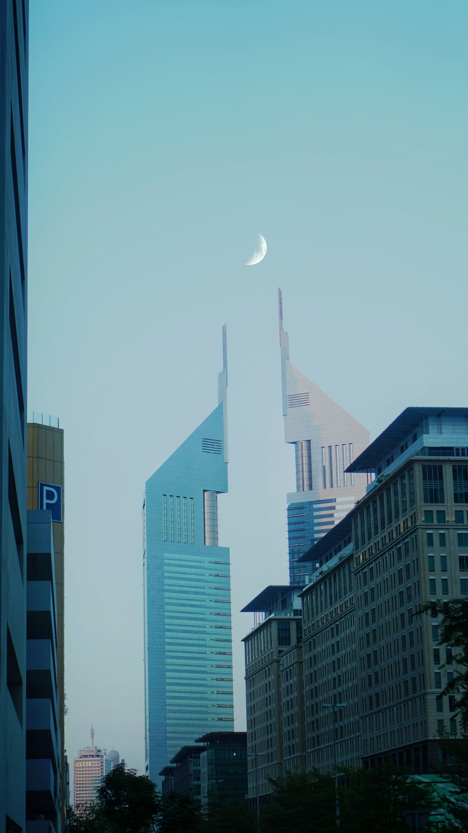 Emirates Towers in Dubai against a pale evening sky with a crescent moon